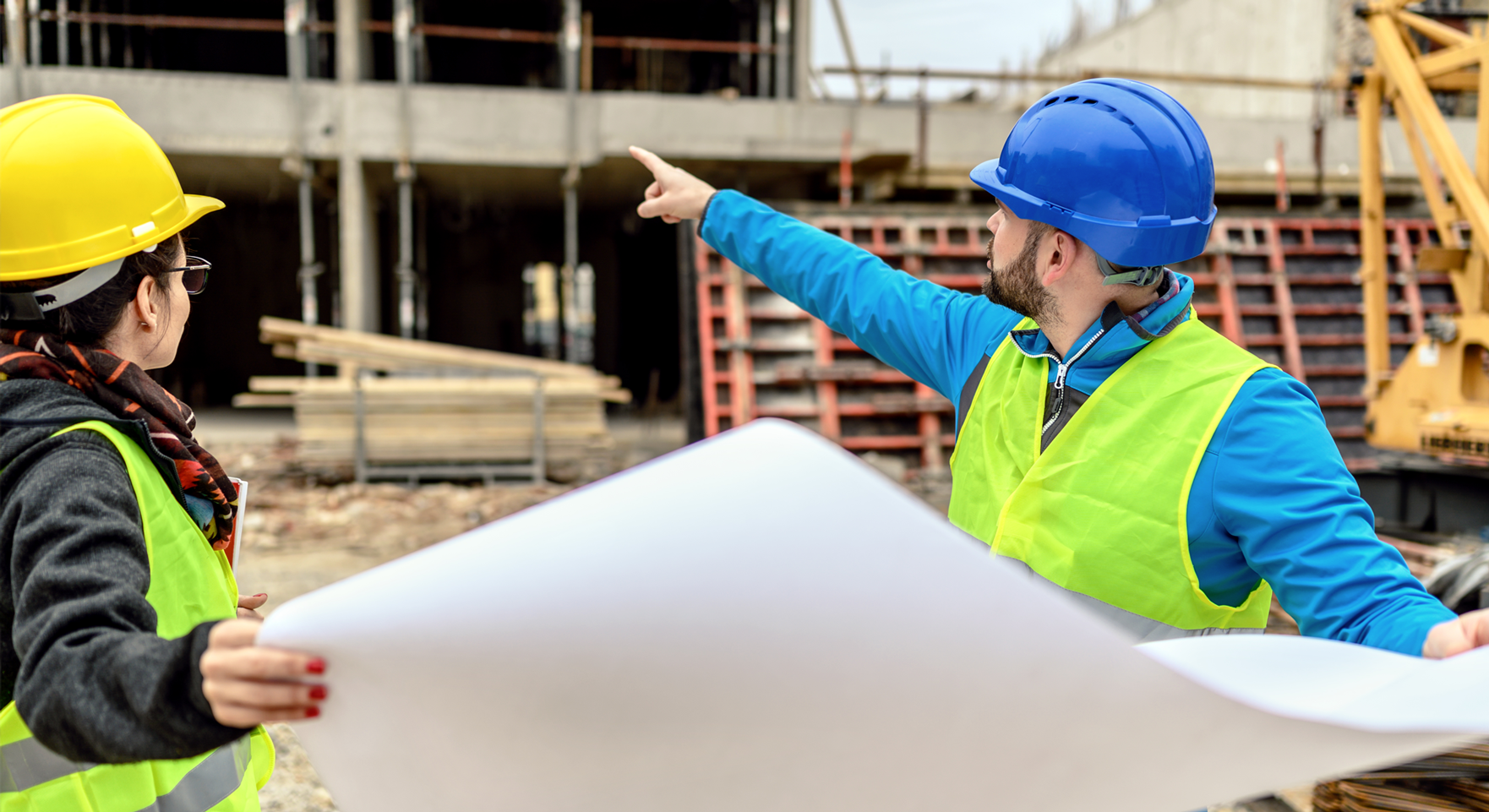 A pair of construction workers looking at a building site and plans