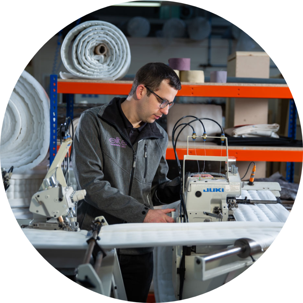 Man in grey overall standing over machine in workshop