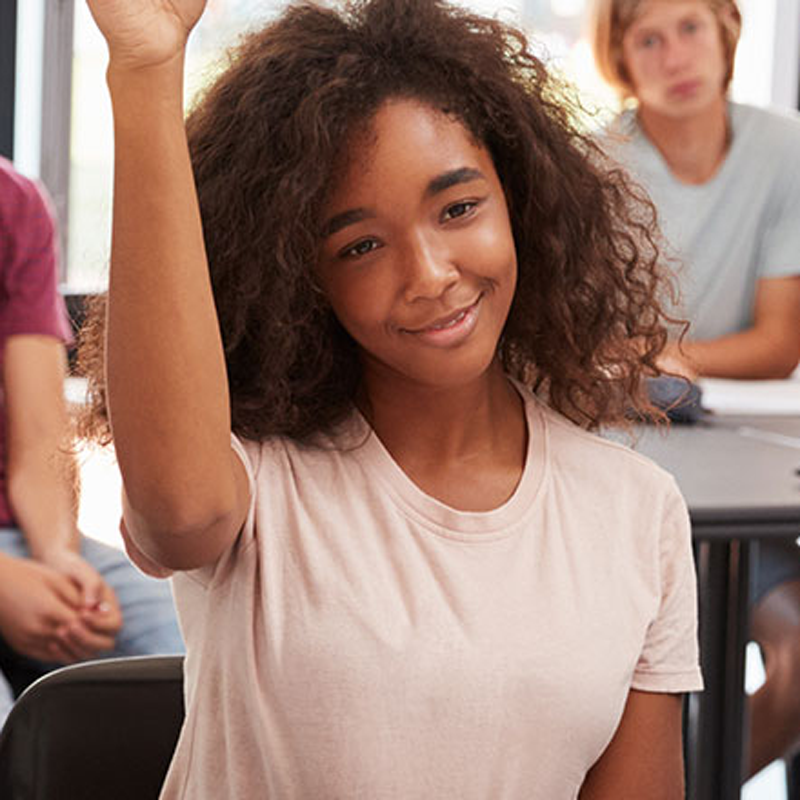 A young person holding their hand in the air in a classroom