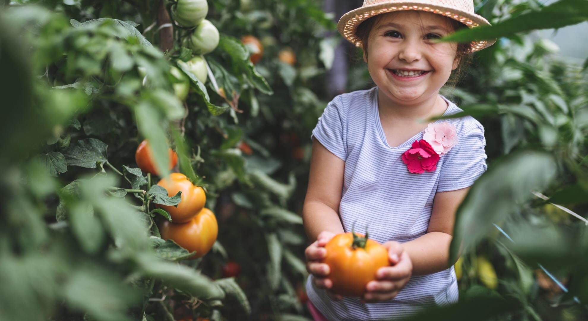 A young child holding vegetables surrounded by green growth in a garden