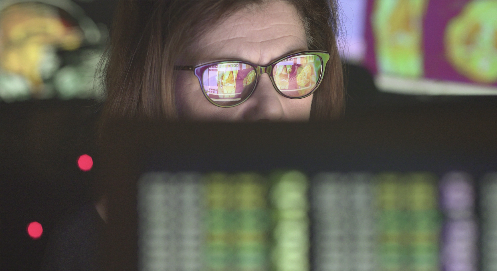 A person with glasses sitting in from of a computer screen showing data