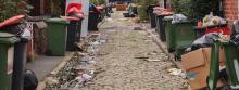 Bins line a cobbled street with rubbish on the ground