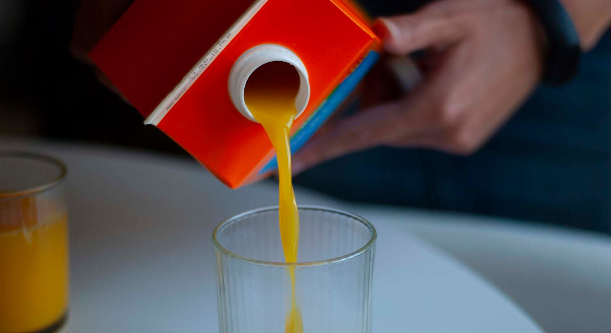 Person pouring orange juice from a drinks carton into a glass