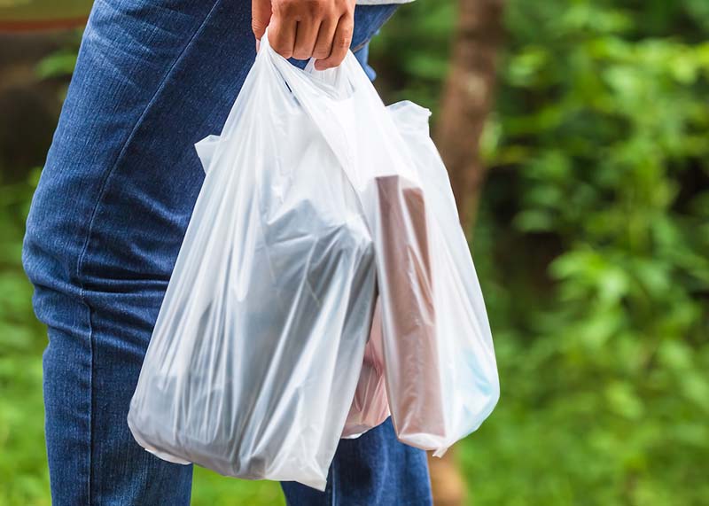  Person walking past greenery carrying plastic carrier bags