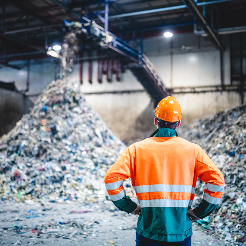 A person standing in front of piles of recycled material at a material recovery facility