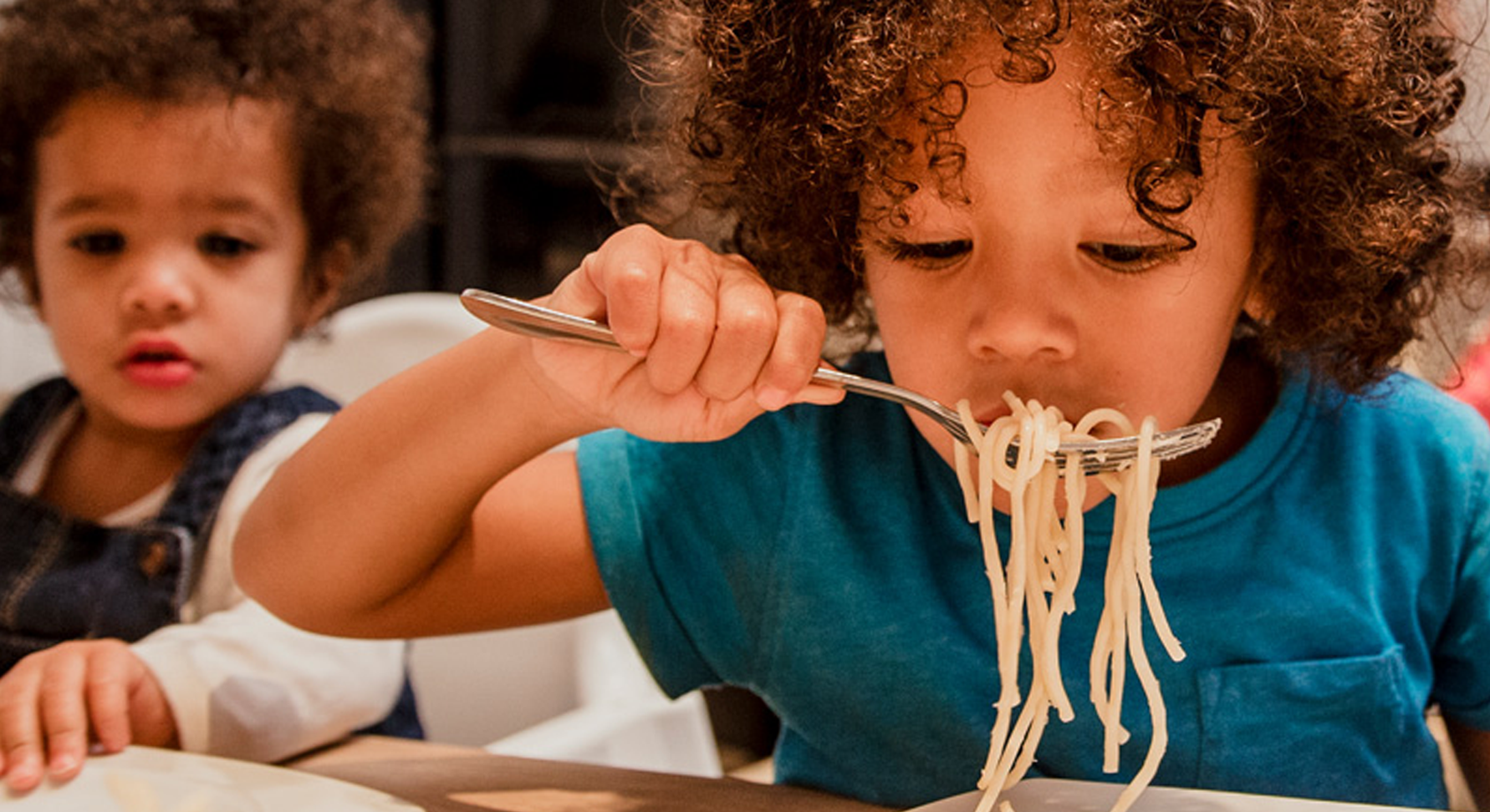 Two young children eating a plate of spaghetti pasta