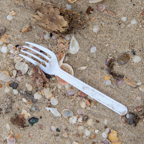 a single use plastic fork on a sandy beach