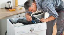 A man is fixing a washing machine in a kitchen