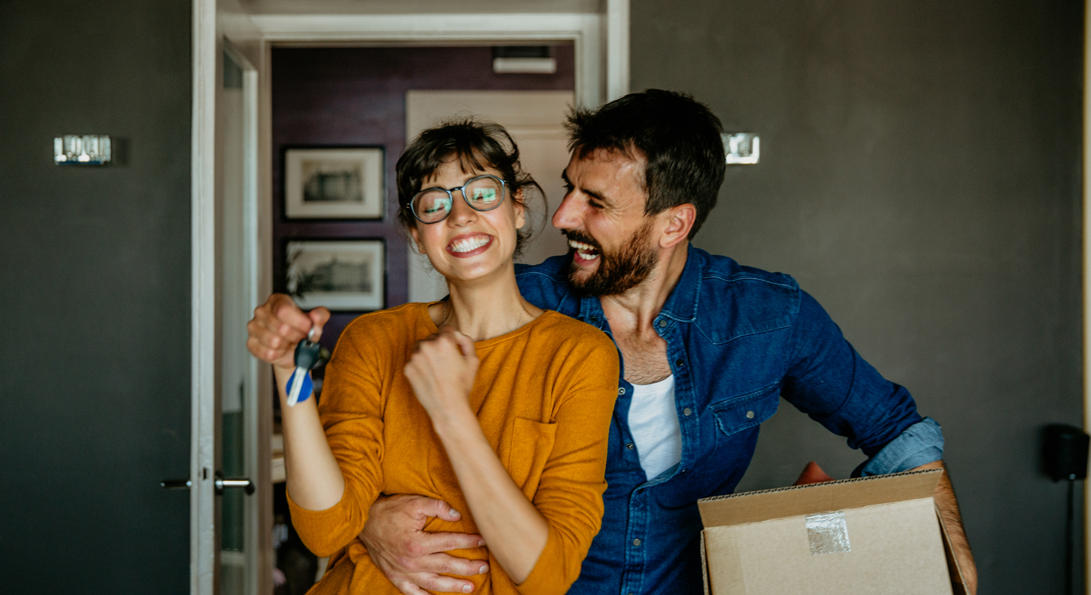 A smiling couple holding a box and key