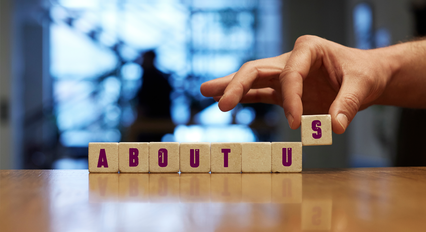 An abstract image of a hand placing wooden blocks with letters to spell 'about us'