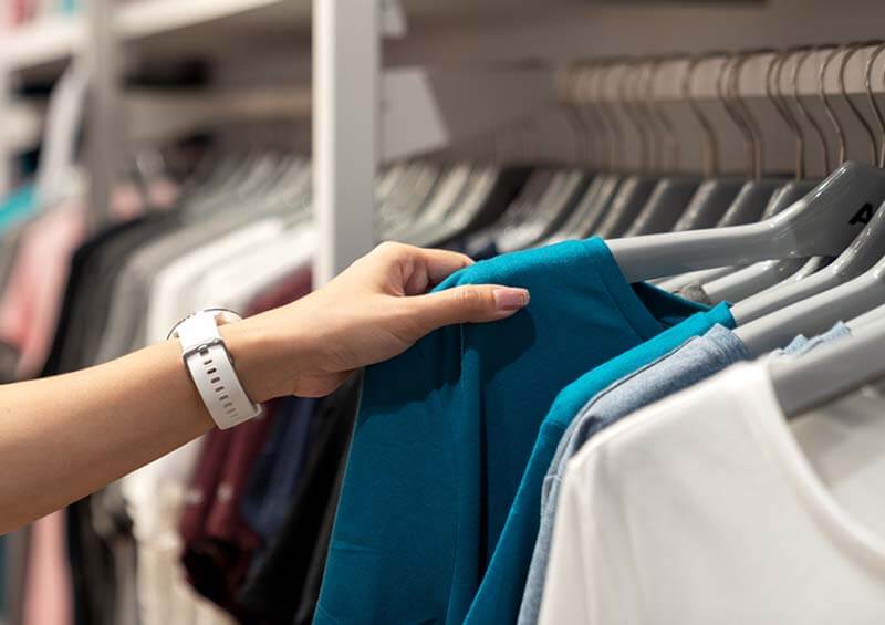 Person lifting a t-shirt from a clothing rail in a fast fashion store