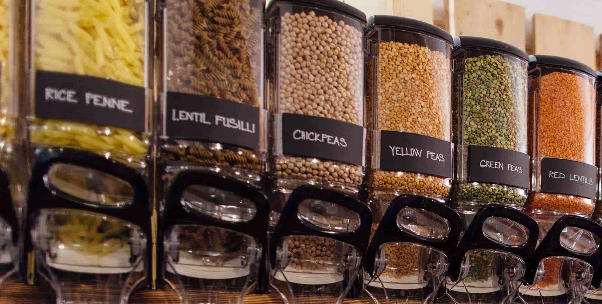 Photo of a row of zero waste store dispensers filled with pasta, chickpeas and lentils.