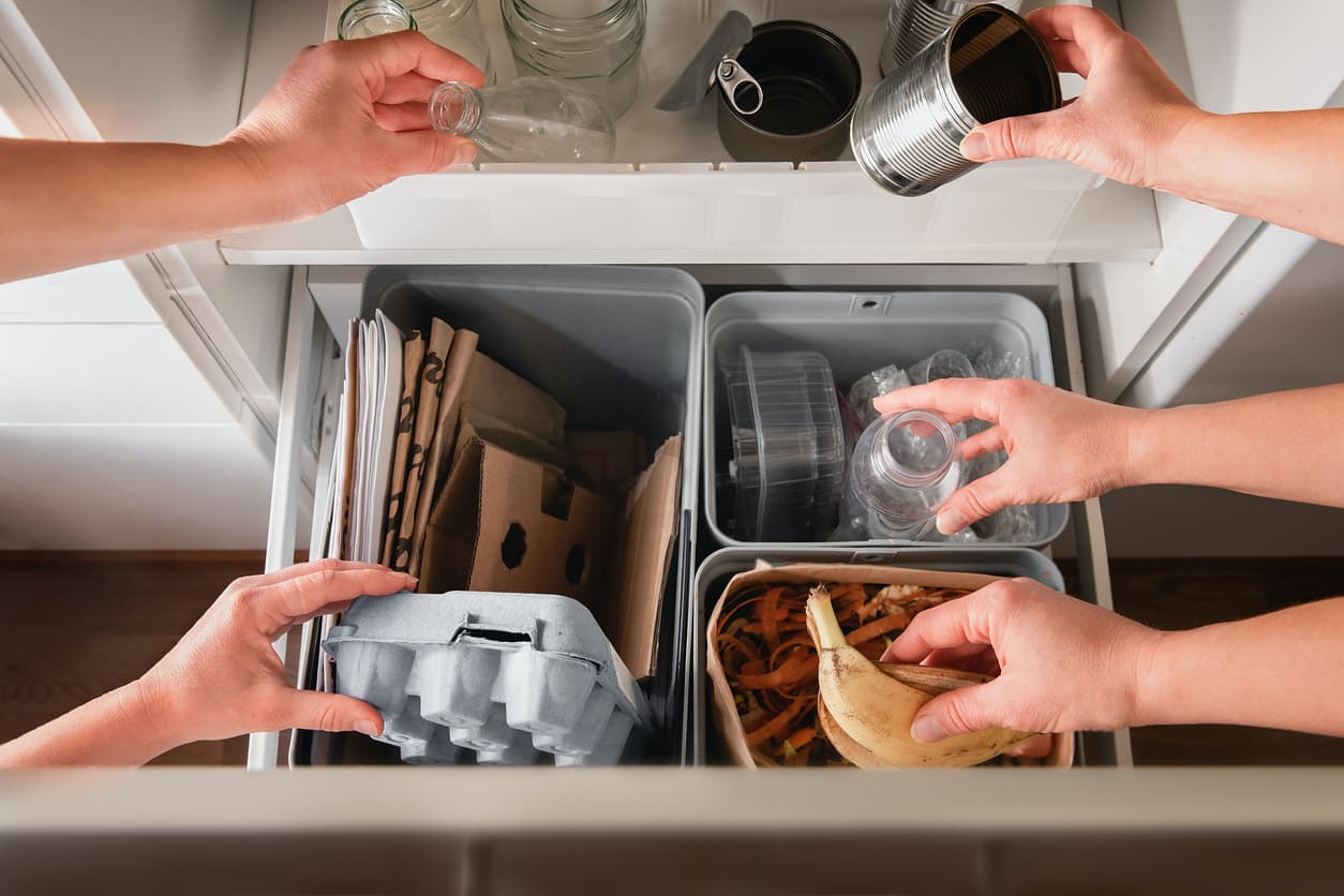 Hands putting segregated household waste to separate bins in kitchen cabinet - plastic, cardboard and paper, bio, metal and glass. Separating waste. 